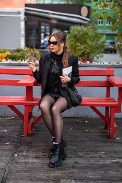 beautiful well-groomed cute young girl enjoys coffee in her favorite autumn city. Autumn concept. City concept. The concept of city walks - Photo, Image