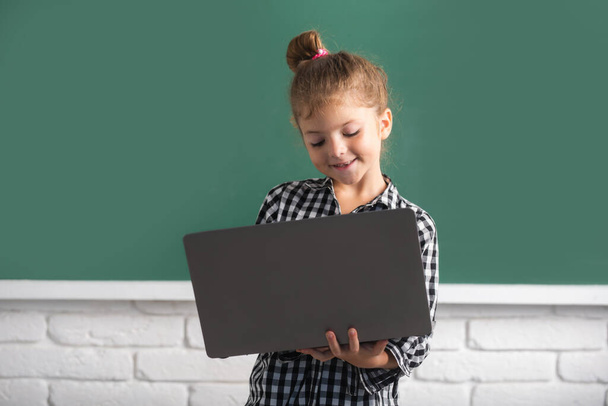 Child girl using a laptop computer at school near blackboard. - Foto, afbeelding