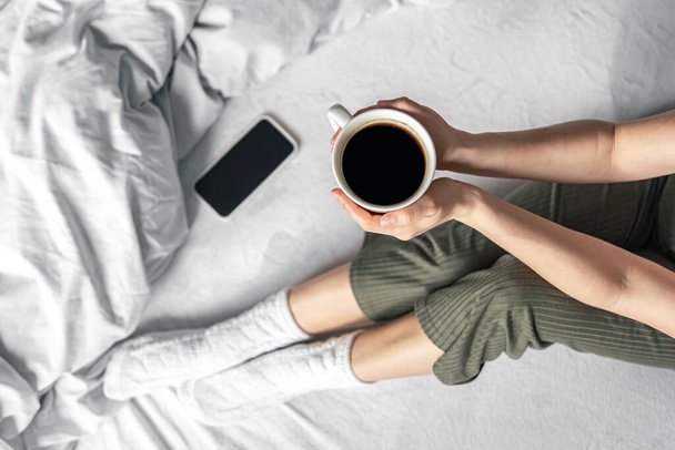 Cup of coffee in bed in female hands, top view. - Photo, Image