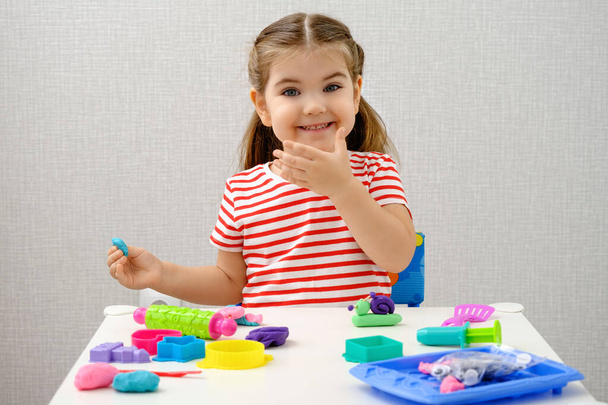 uśmiechnięta dziewczynka bawiąca się kolorową plastycyną, gliną, grać w ciasto na białym stole, domowe gry edukacyjne, szczęśliwa koncepcja dzieciństwa - Zdjęcie, obraz