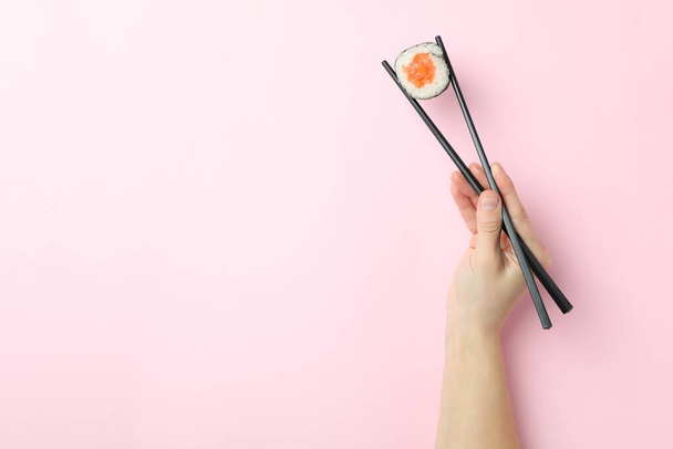 Женская рука держит суши с палочками на розовом фоне - Фото, изображение