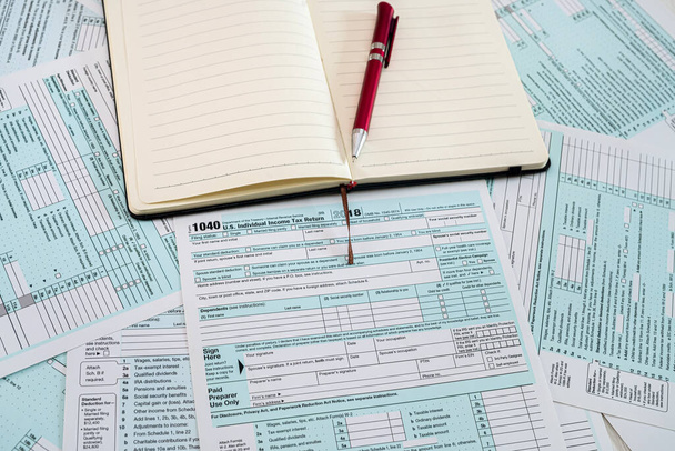 Новые налоговые формы США 1040 с красной ручкой и блокнотом разложены на столе. Концепция документации - Фото, изображение
