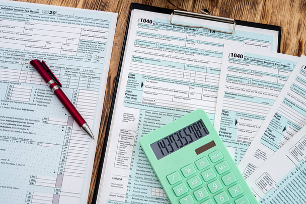 nuevos formularios de impuestos 1040 usa con una calculadora verde con un bolígrafo rojo esparcido en una mesa de madera. Concepto de documentación - Foto, Imagen