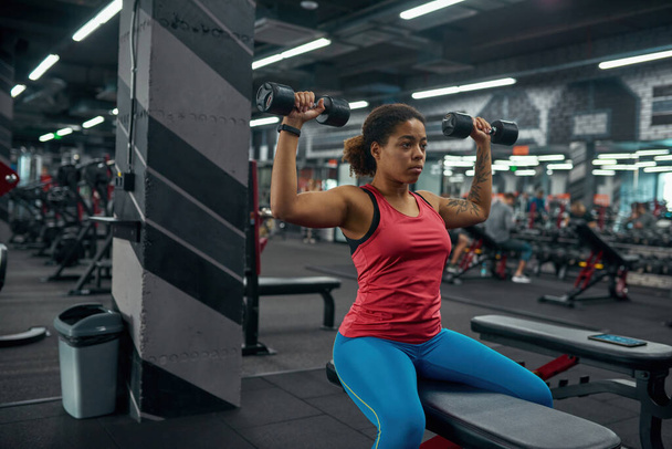Black girl doing exercise with dumbbells in gym - Photo, image