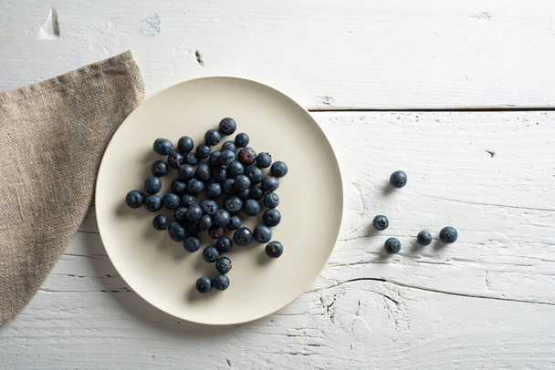 plate with blueberries and linen napkin on whitewashed wooden table - Zdjęcie, obraz