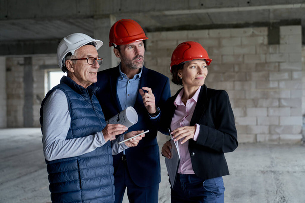Keskikokoinen kuva valkoihoisten insinöörien ja sijoittajien ryhmästä seisomassa ja keskustelemassa rakennustyömaalla  - Valokuva, kuva