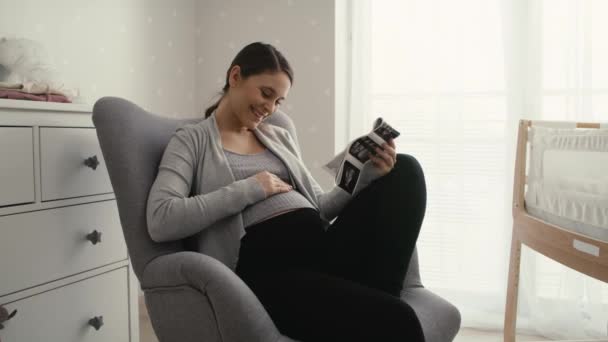 Mid shot video van blanke vrouw in geavanceerde zwangerschap browsen echografie scan in baby 's kamer. Opgenomen met RED helium camera in 8K. - Video