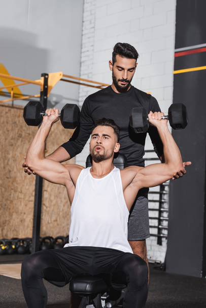 Arabe entraîneur debout près du sportif avec haltères dans la salle de gym  - Photo, image