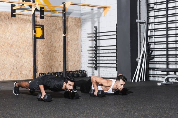 Multiethnic sportsmen doing press ups with dumbbells in gym  - Foto, Imagen