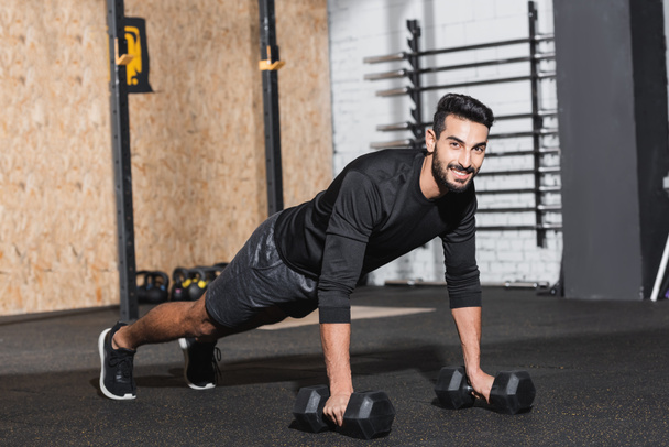 Smiling arabian sportsman training with dumbbells in sports center  - Foto, immagini