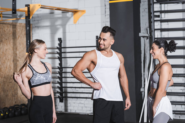 Positive sportsman standing near multiethnic sportswomen in gym  - Photo, Image