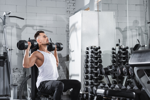 Young man in sportswear lifting dumbbells in gym  - Фото, зображення