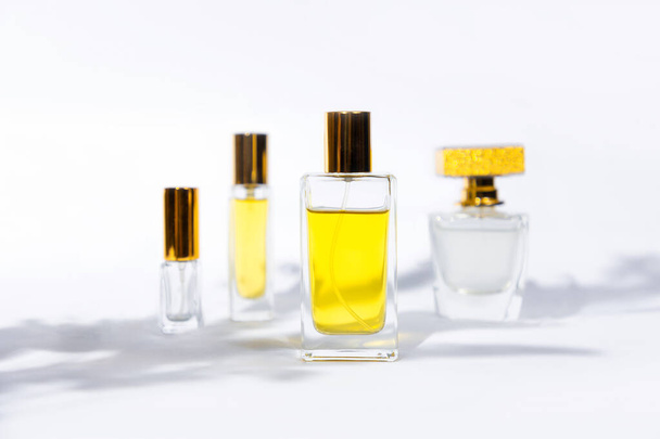 Vier transparente rechteckige Glasflaschen mit goldenem Parfüm auf weißem Hintergrund mit Sonnenlicht und Blätterschatten. Vorlage für Parfümerie im minimalen Stil. Kopierraum - Foto, Bild