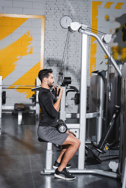 Side view of arabian man training with lat pulldown machine in gym  - Фото, зображення