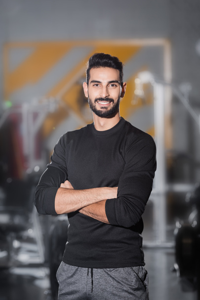 młody arabski sportowiec uśmiecha się do kamery w zamazanej siłowni  - Zdjęcie, obraz