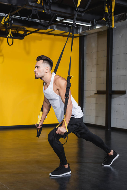 Young sportsman training with suspension straps in sports center  - Photo, Image