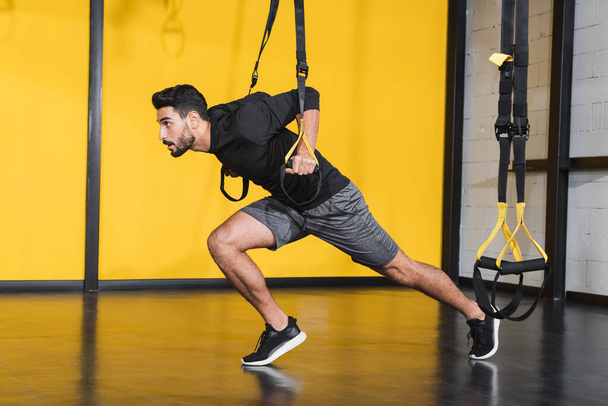 Side view of muslim sportsman working out with suspension straps in gym  - Φωτογραφία, εικόνα