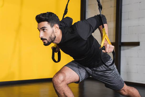 Bearded arabian sportsman pulling suspension straps in gym  - Foto, Bild