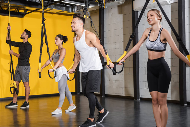 Positive interracial people training with suspension straps in gym  - Foto, afbeelding