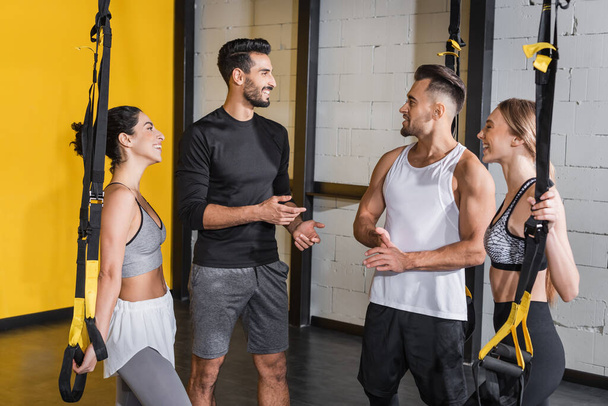 Smiling interracial people talking near suspension straps in gym  - Photo, Image