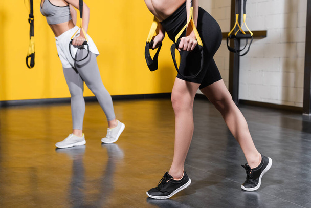 Cropped view of fit sportswoman pulling suspension straps in gym  - Fotó, kép