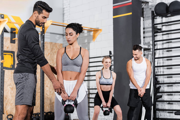 Muslim trainer pointing at kettlebell near middle east sportswoman in gym  - 写真・画像