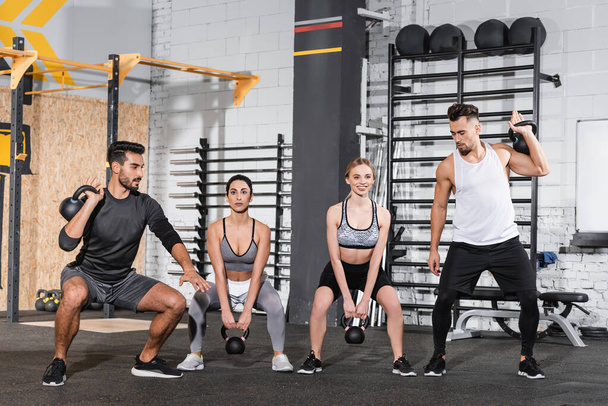 Smiling multiethnic people training with kettlebells in sports center  - Photo, Image