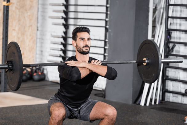 Arabian sportsman training with barbell in blurred sports center - Photo, image