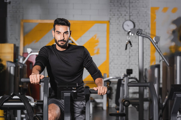 Muslim sportsman looking at camera while training on elliptical trainer - Foto, immagini