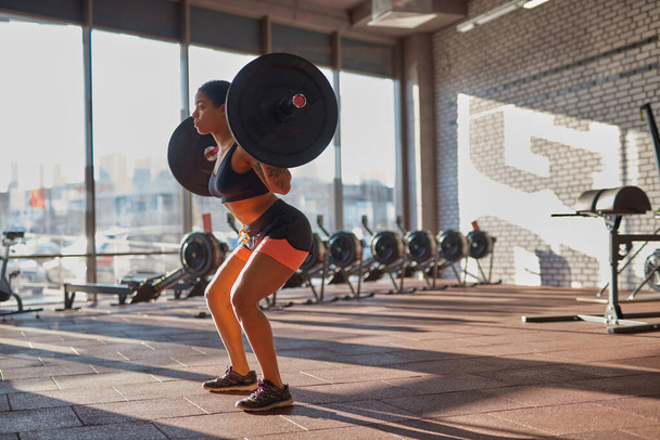 Black girl do sit ups with barbell in sport club - 写真・画像