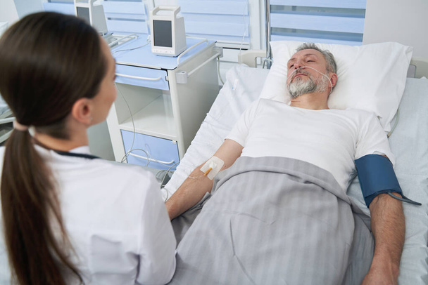 Calm patient undergoing intravenous therapy supervised by doctor - Foto, imagen