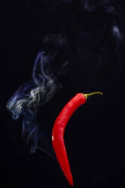 Красный острый перец чили на черном фоне с дымом, идущим из него, изображая его горячим дымом - Фото, изображение
