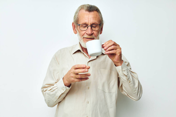 elderly man drinking from a mug on a white background and smiling - Foto, Bild