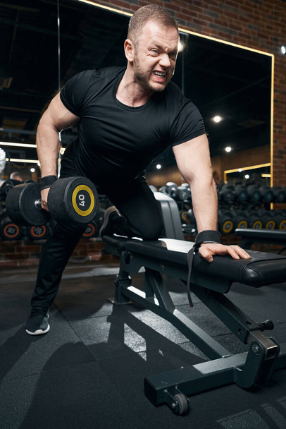 Professional sportsman performing single-arm bent-over row in gym - Fotó, kép