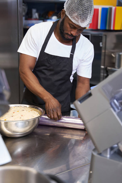 Mies mustassa esiliinassa valmistelee ainesosia keittiössä - Valokuva, kuva