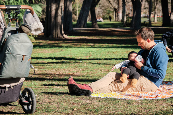 Young man bottle feeding her son outdoors in a public park - Foto, Imagem