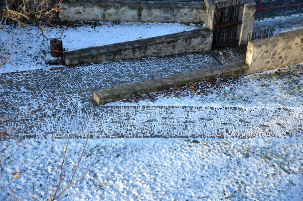 σκάλες και ράμπες για αναπηρικά καροτσάκια από όμορφο σκυρόδεμα. πέτρινες επιφάνειες από πλακόστρωση και σκάλες φωτισμένες από τον ήλιο. Χαλασμένο χαλύβδινο κάγκελο. αυλή μεσαιωνική το χειμώνα ορθογώνιο μονοπάτι - Φωτογραφία, εικόνα