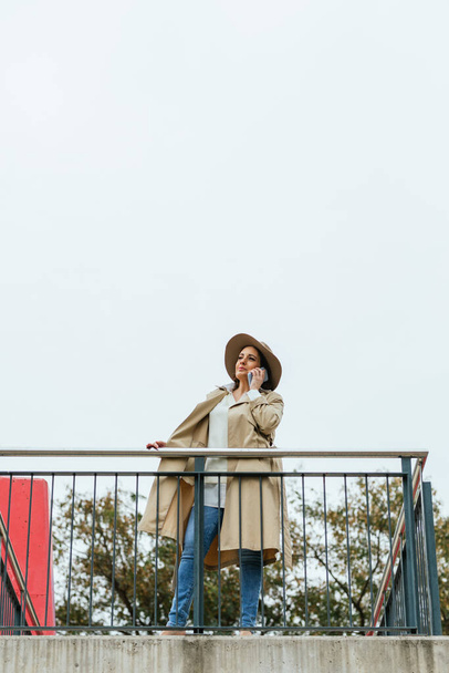 An adult woman leaning on a railing talking on her cell phone - Fotó, kép