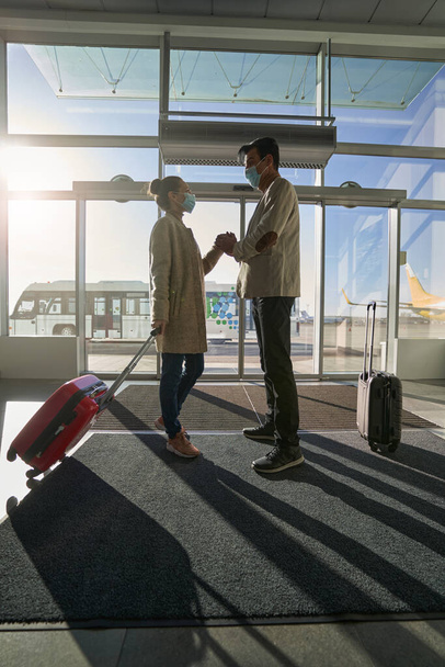 man sluiten vrouw hand in zijn handpalmen in de buurt luchthaven deur - Foto, afbeelding