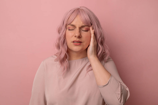 Przystojny różowe włosy kobieta stoi z ręką na głowie na ból w głowie, ponieważ stres na odizolowanym różowym tle. Cierpi na migrenę. Koncepcja zdrowia i stresu - Zdjęcie, obraz