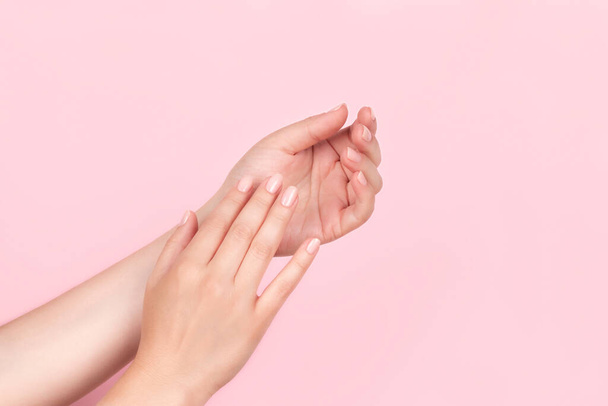 Samičí ruce s krásnou přírodní manikúrou - růžové nahé nehty na růžovém pozadí. Koncept péče o nehty - Fotografie, Obrázek
