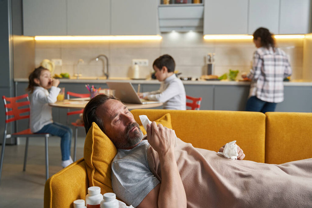 Father lying with sickness on couch and blowing his nose - Foto, imagen