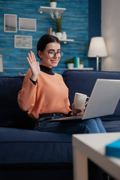 Influencer with glasses sitting on couch holding cup and laptop on lap. - Foto, Imagem