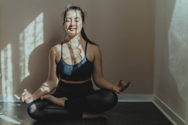 Young woman in meditative position practicing yoga at home - beautiful girl meditates sukhasana posture relaxation - healthy lifestyle body and mind concept - 写真・画像