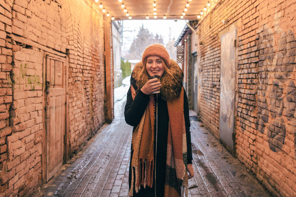 Молодая женщина в шляпе, перчатках, с одноразовой чашкой горячего напитка зимой. - Фото, изображение