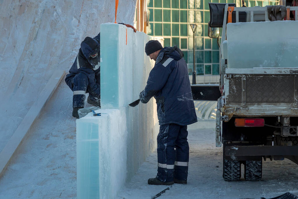 Двоє робітників покривають каркас дерев'яної гірки льодовими панелями
 - Фото, зображення