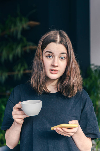 Teenage girl with a cup of tea and a smartphone in her hands. - Foto, Imagem