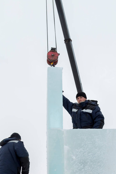 Δύο εργαζόμενοι καλύπτουν το πλαίσιο μιας ξύλινης τσουλήθρας με πλάκες πάγου - Φωτογραφία, εικόνα