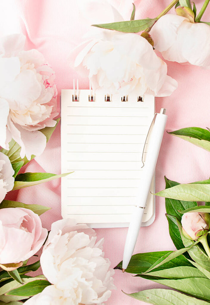 A frame of white and pink peonies and a notepad on a pink fabric background. Floral spring or summer concept. Flat layout. View from above. Copy space. Place for text. - Photo, Image