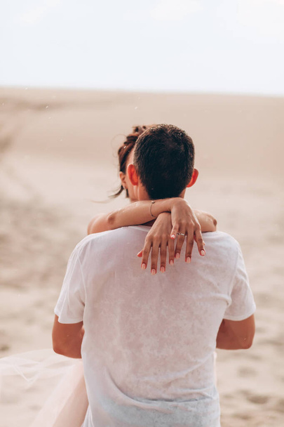 mujer joven abrazando a un hombre joven en la lluvia en el desierto en la playa - Foto, Imagen